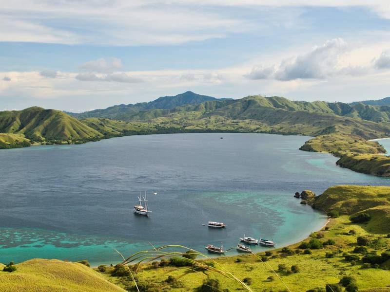 Boats in a bay surrounded by green hills in Komodo, Indonesia